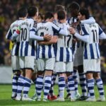Jugadores de la Real Sociedad se abrazan en grupo sobre el césped.