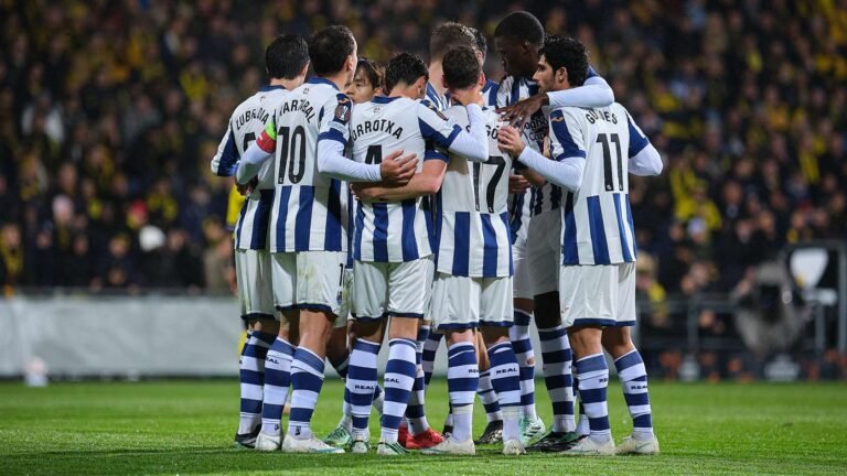 Jugadores de la Real Sociedad se abrazan en grupo sobre el césped.
