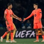 Dos jugadores del Barcelona con equipación naranja se acercan con las manos extendidas durante el partido.