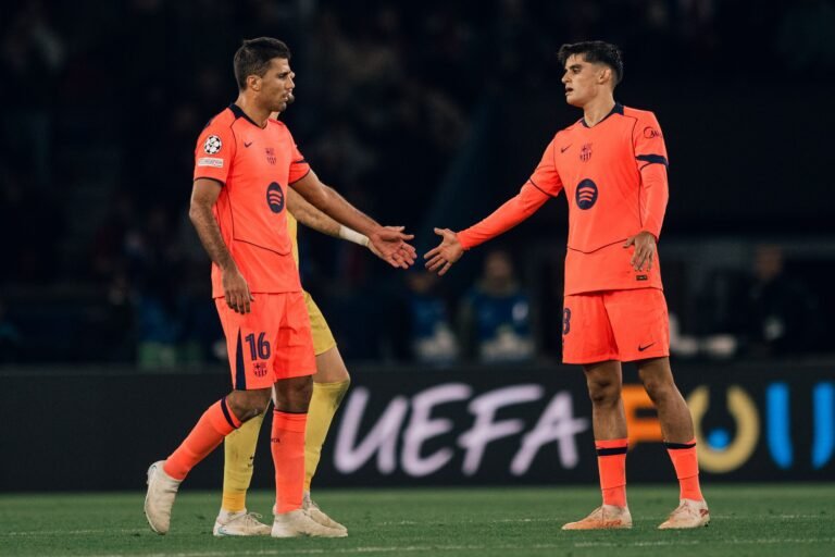 Dos jugadores del Barcelona con equipación naranja se acercan con las manos extendidas durante el partido.