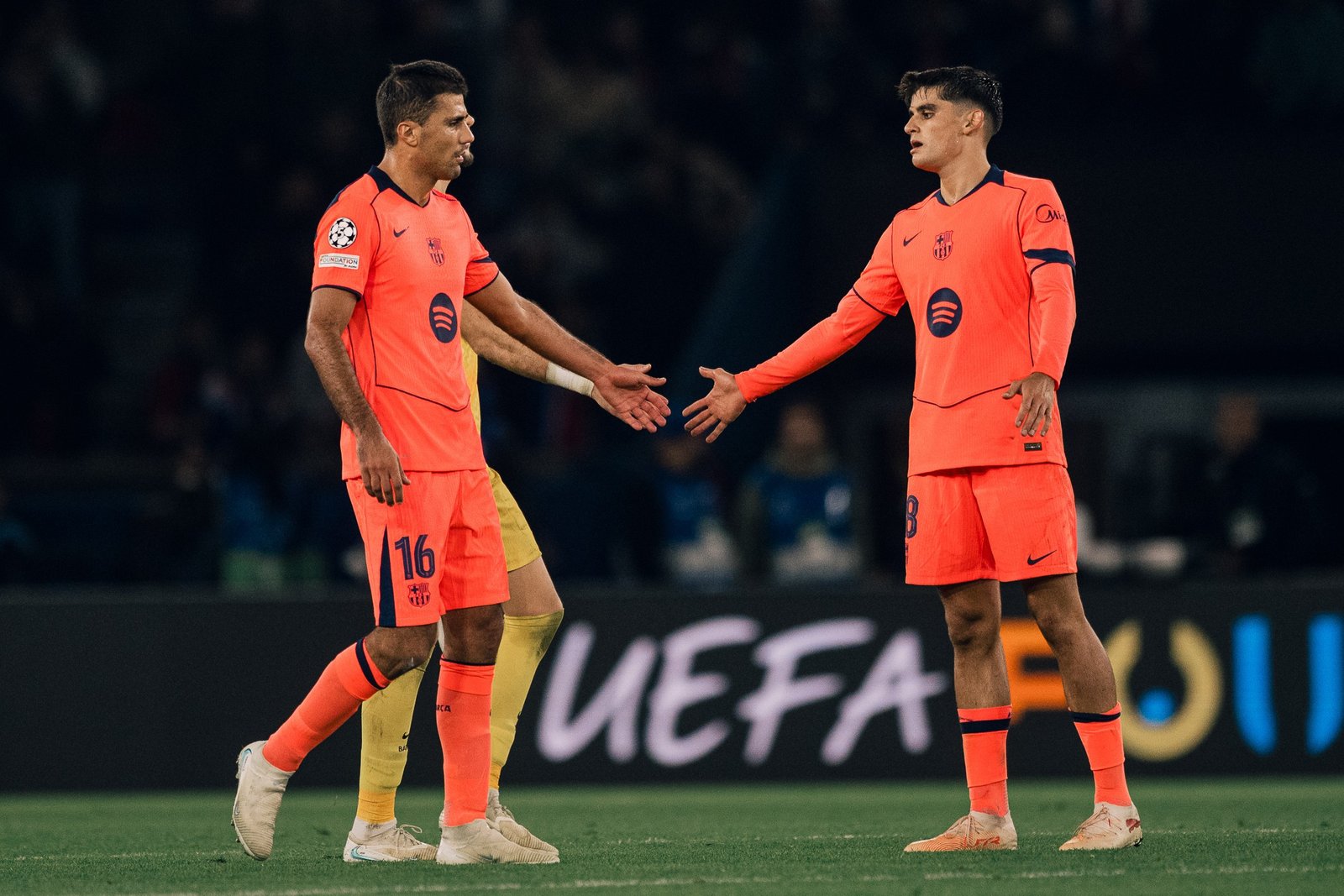Dos jugadores del Barcelona con equipación naranja se acercan con las manos extendidas durante el partido.