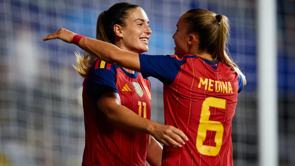 Dos futbolistas de España se abrazan; una viste la camiseta de Medina con el dorsal 6