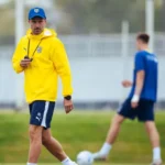 Persona con sudadera amarilla del Parma durante un entrenamiento, con futbolistas al fondo