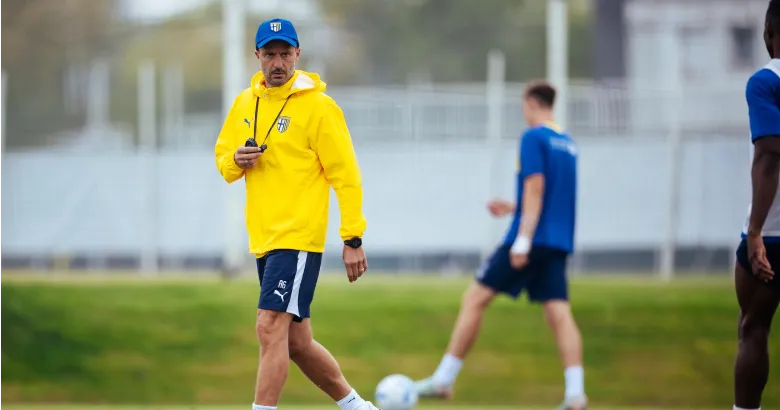 Persona con sudadera amarilla del Parma durante un entrenamiento, con futbolistas al fondo