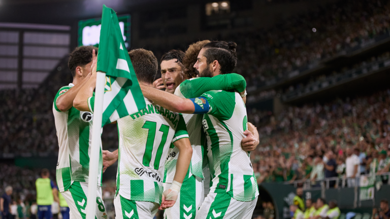Varios jugadores del Betis se abrazan junto a un banderín de córner.