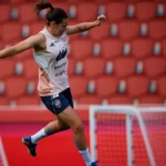 Futbolista entrenando con un balón ante una grada de asientos rojos