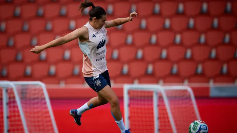 Futbolista entrenando con un balón ante una grada de asientos rojos