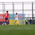 Futbolista de España conduce el balón frente a un rival vestido de rojo.