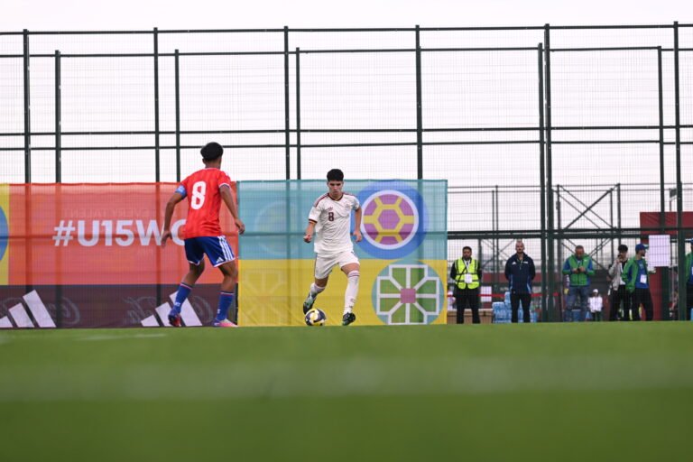 Futbolista de España conduce el balón frente a un rival vestido de rojo.