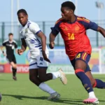 Futbolista de España con el dorsal 14 corre junto a un rival vestido de blanco.