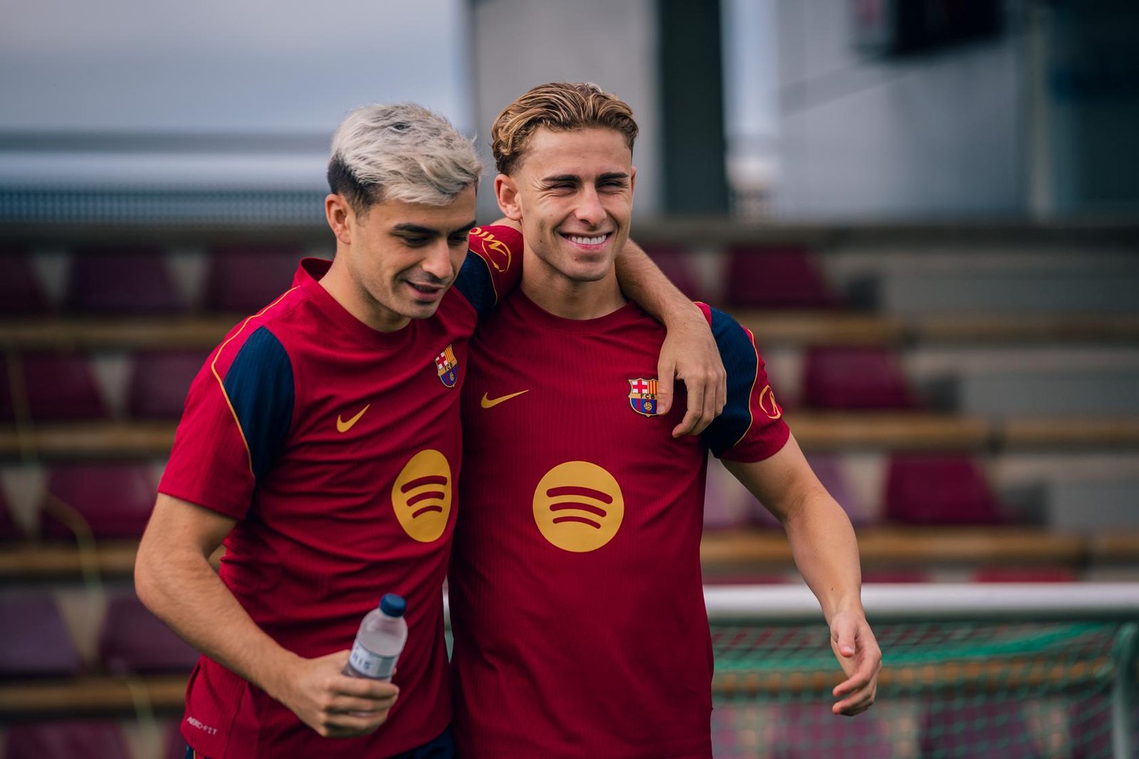 Dos jugadores del FC Barcelona caminan abrazados con ropa de entrenamiento.