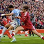 Jugador del Manchester City disputa el balón con futbolistas del Liverpool en Anfield